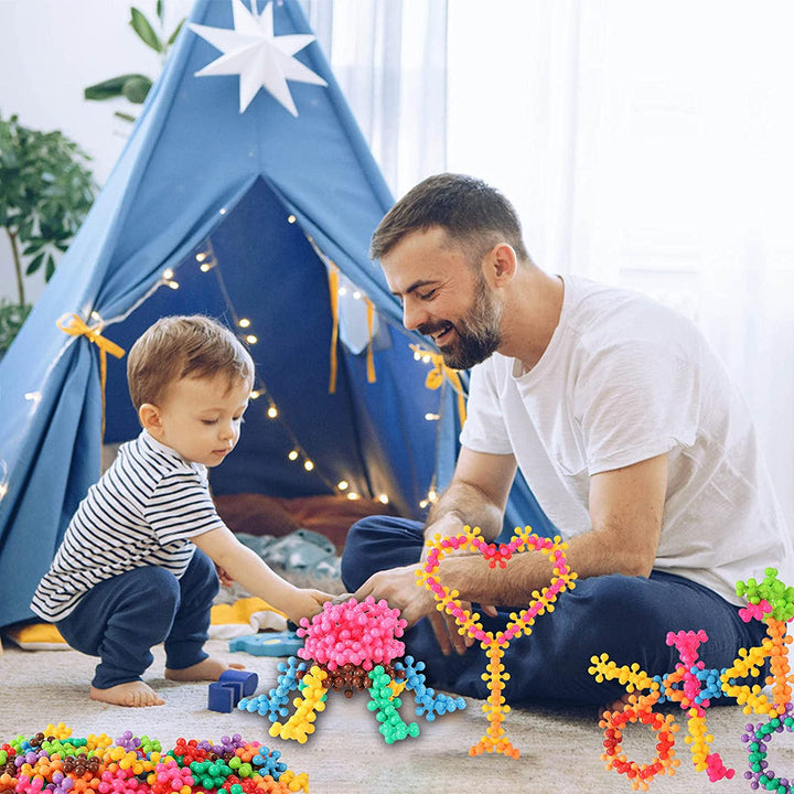 Adult and child building colorful models together with snowflake-shaped blocks