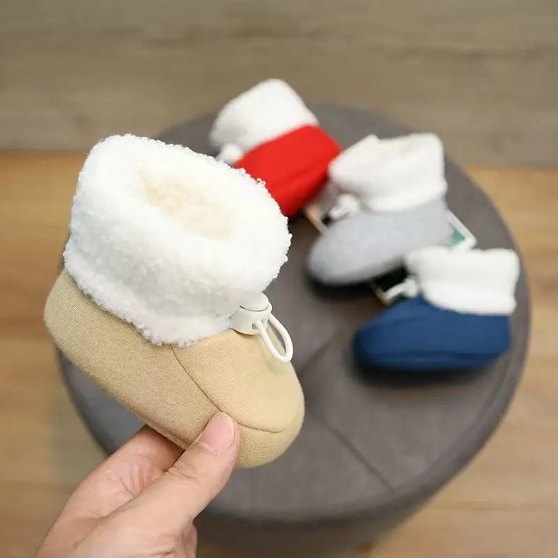 Apricot baby winter boot with a fluffy white cuff, with red, gray, and blue boots in the background