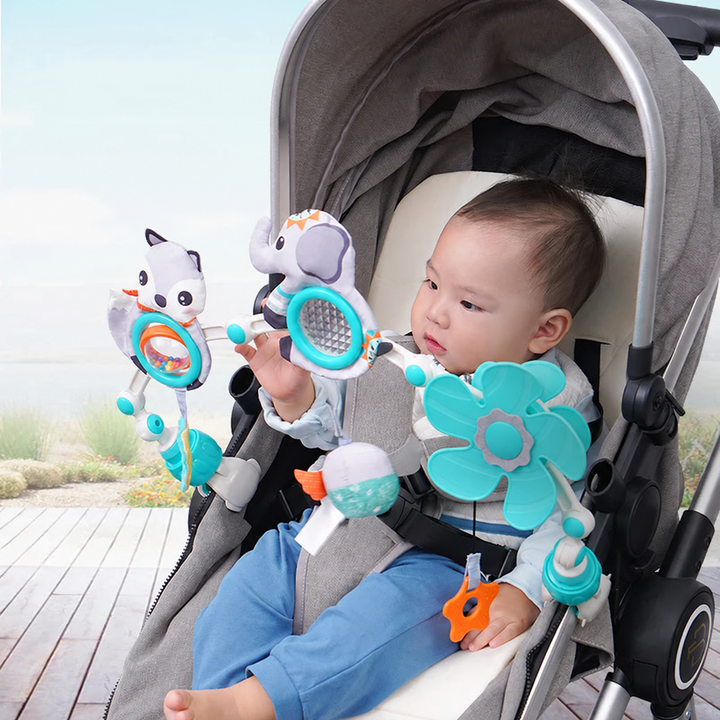 Baby reaching toward the colorful toys on an arch clipped to a stroller