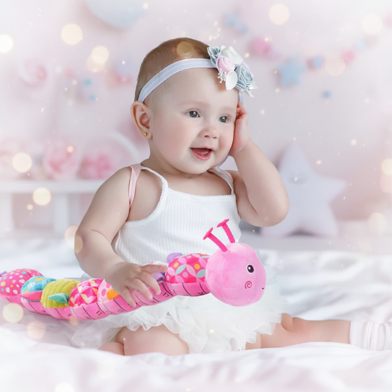 Baby holding a pink caterpillar rattle across their lap