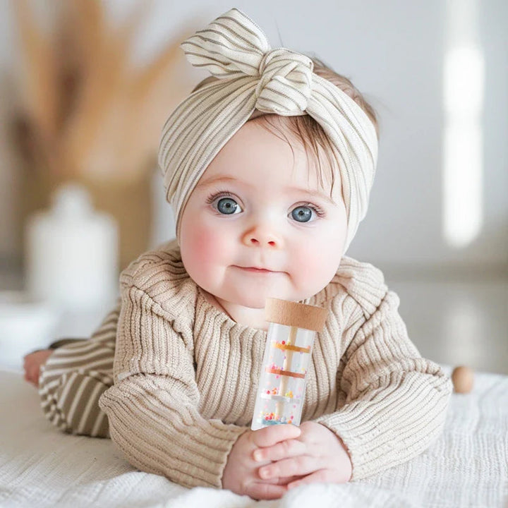 Baby in a knit sweater holding a rainstick rattle with wooden ends
