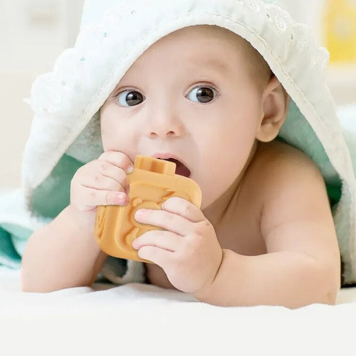 Baby holding and mouthing an orange textured stacking cube