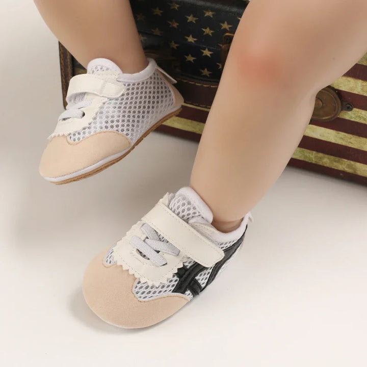 Baby wearing cream sneakers with mesh panels and wide strap closures