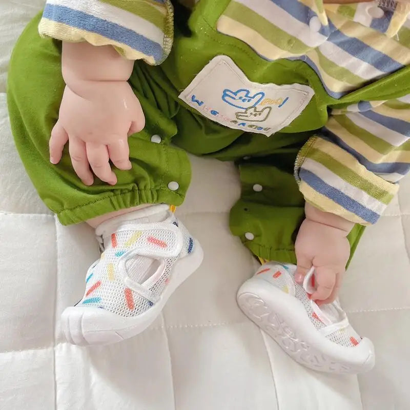 Baby wearing white printed mesh sandals with green overalls
