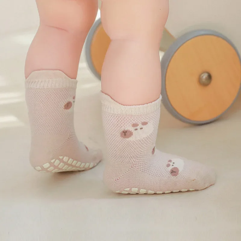 Child standing in beige bear-pattern grip socks beside a wooden wheeled toy.