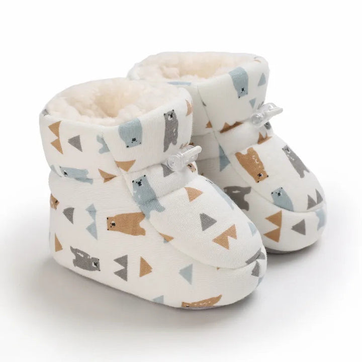 Angled view of cream baby slippers patterned with bears and triangles