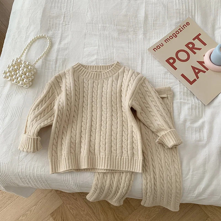 Beige cable-knit sweater with ribbed neckline and cuffs, paired with matching pants