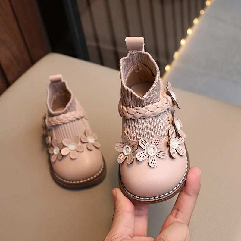 Beige ankle boot held up to show raised flowers, braided trim, and a ribbed ankle cuff.