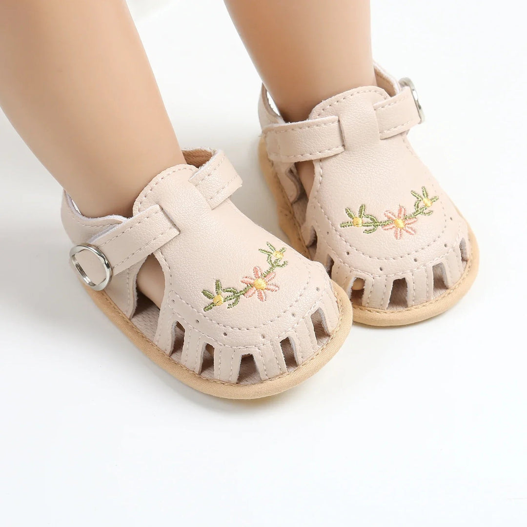 Beige embroidered baby sandals showing T-straps, side openings and light-colored soles