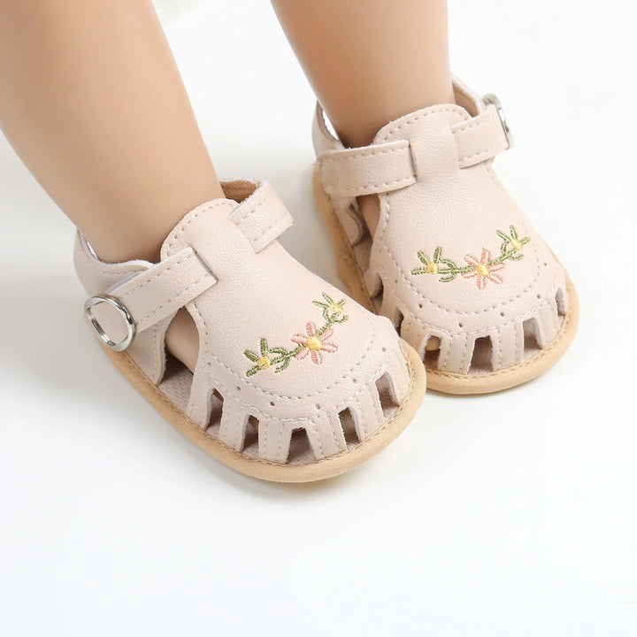 Beige embroidered baby sandals showing T-straps, side openings and light-colored soles
