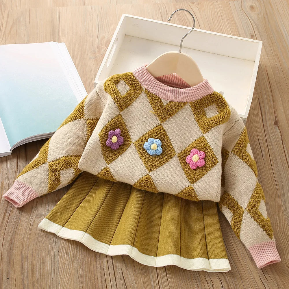 Beige diamond-knit sweater with pink trim and raised flowers, paired with a mustard-colored pleated skirt