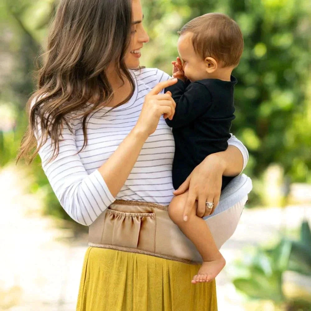 Adult holding a baby on a beige hip carry seat outdoors