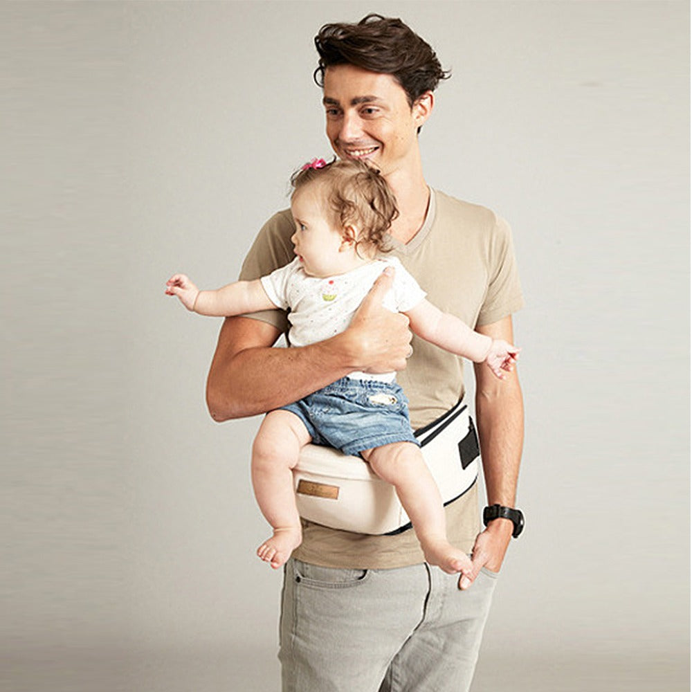 Adult supporting a baby seated on a beige hip carry seat