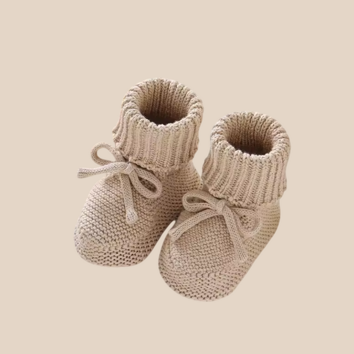 Beige knitted baby booties with ribbed fold-over cuffs and bow ties