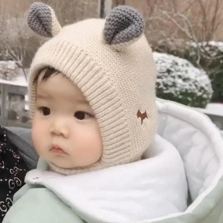 Baby outdoors in a beige knit balaclava with gray ears and a ribbed face opening