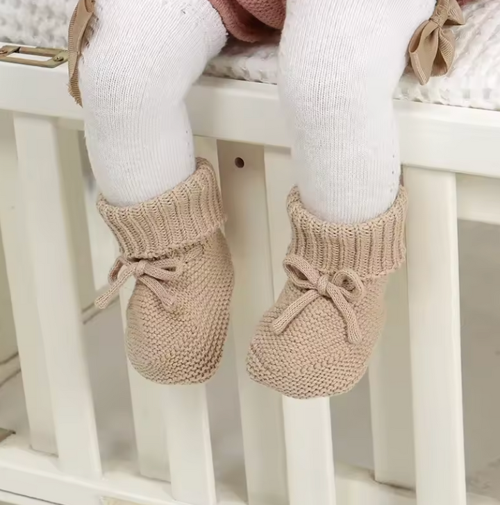 Baby wearing beige knitted booties over white tights