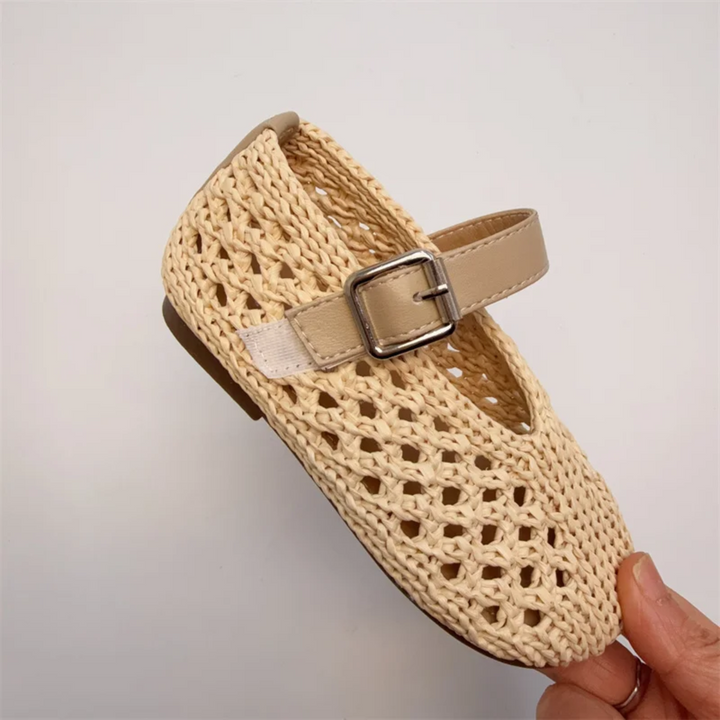 Angled side view of a beige Mary Jane flat with an openwork upper and buckle strap
