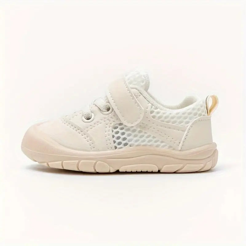 Side profile of a beige mesh baby shoe with an adjustable strap and heel loop