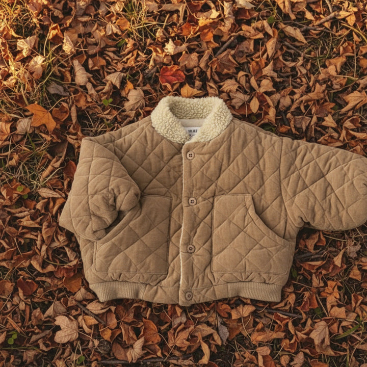 Beige quilted coat with a sherpa collar laid on autumn leaves
