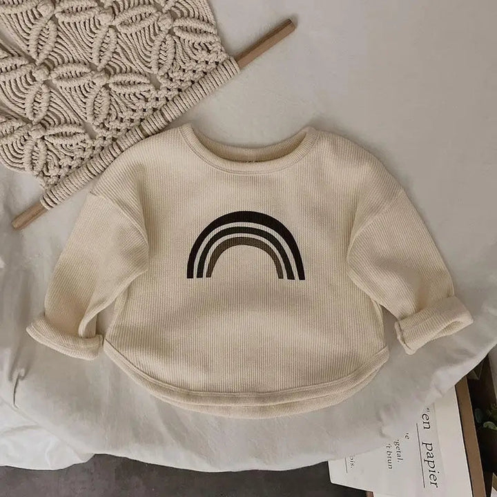 Beige textured rainbow T-shirt laid flat with the sleeves rolled