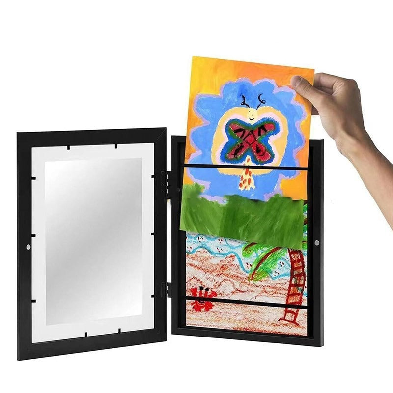 Open black art frame with a hand inserting a colorful drawing above stored artwork