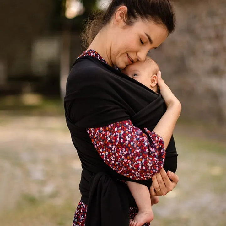 Parent carrying a baby close in a black wrap carrier outdoors.