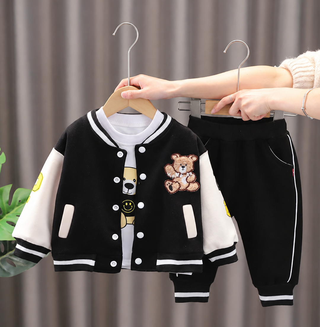 Black-and-white bear-patch varsity jacket, graphic T-shirt, and matching black pants on hangers