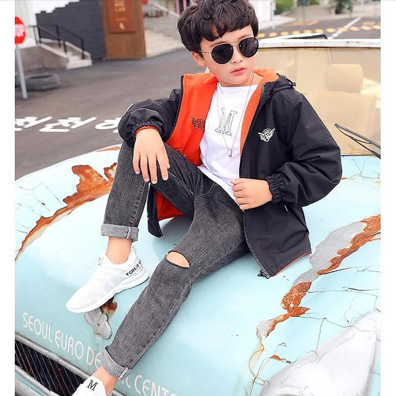 Child seated outdoors wearing a black hooded jacket with orange lining.