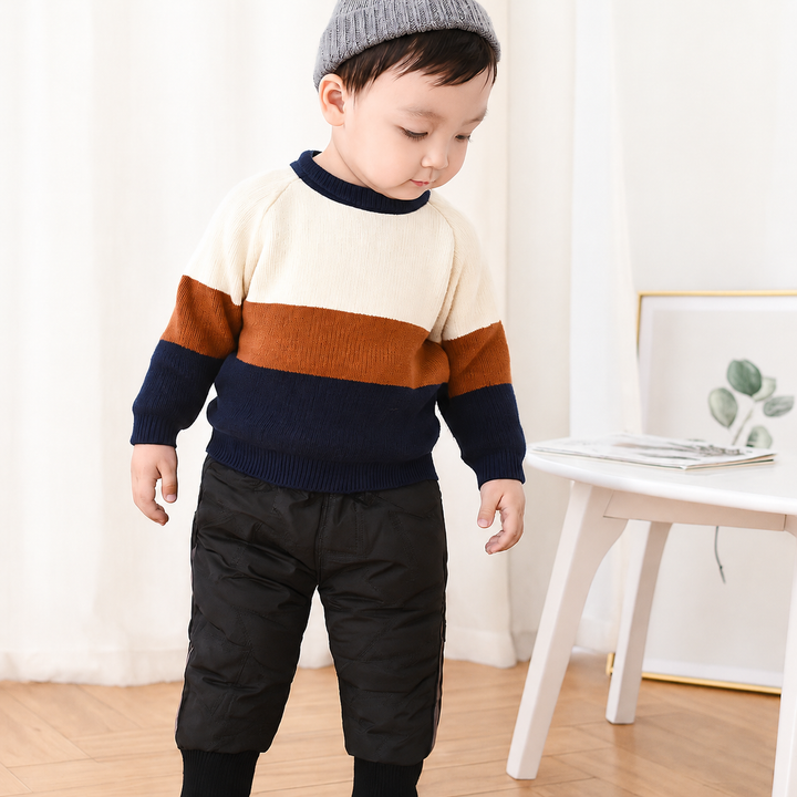 Child wearing black padded winter pants with a striped sweater indoors