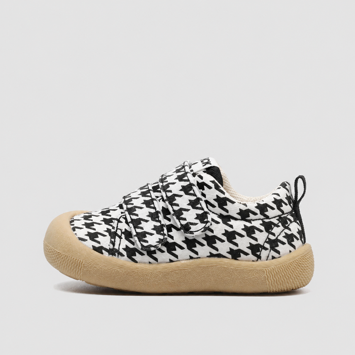 Side view of a black-and-white houndstooth canvas sneaker with a tan sole and strap closure