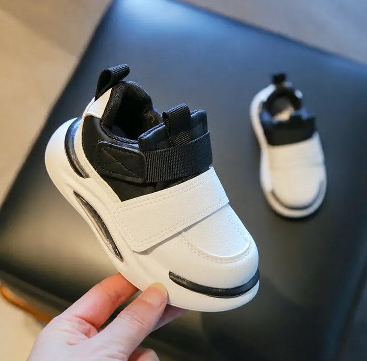 Black and white sneaker held to show the wide strap, toe detail, and collar