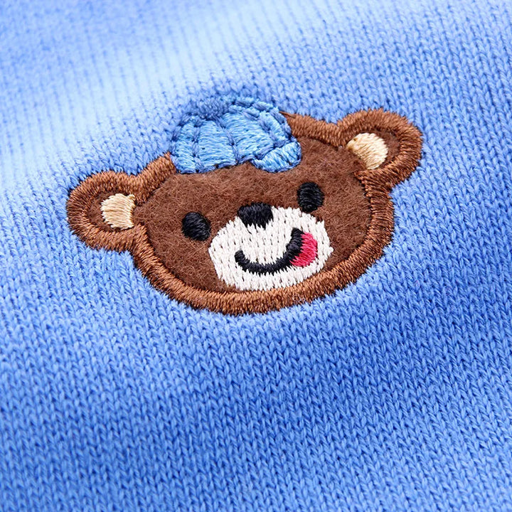Embroidered brown teddy bear with a blue cap on the blue knit cardigan