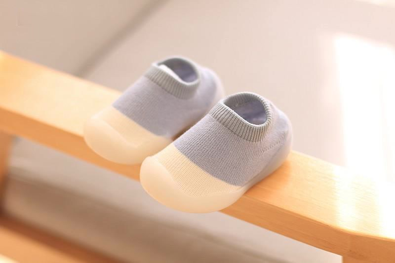 Blue-gray knit baby shoes with cream toes on a wooden rail.