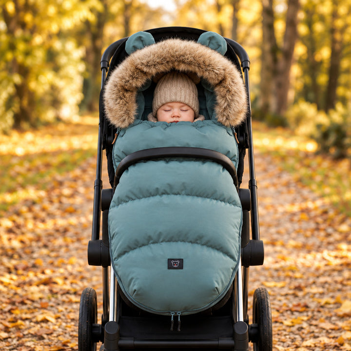 Baby in a blue-green stroller footmuff during an autumn outing