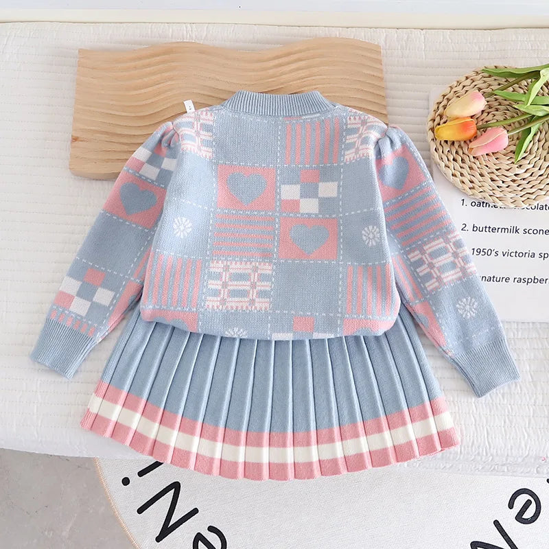 Blue two-piece knit outfit laid flat, showing patterned sleeves and a pleated skirt with pink-and-white hem stripes
