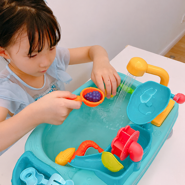 Child using a scoop beneath the running faucet of the blue play sink