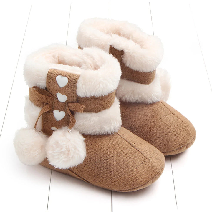 Brown baby snow boots with cream trim, small bows, and fluffy pom-poms