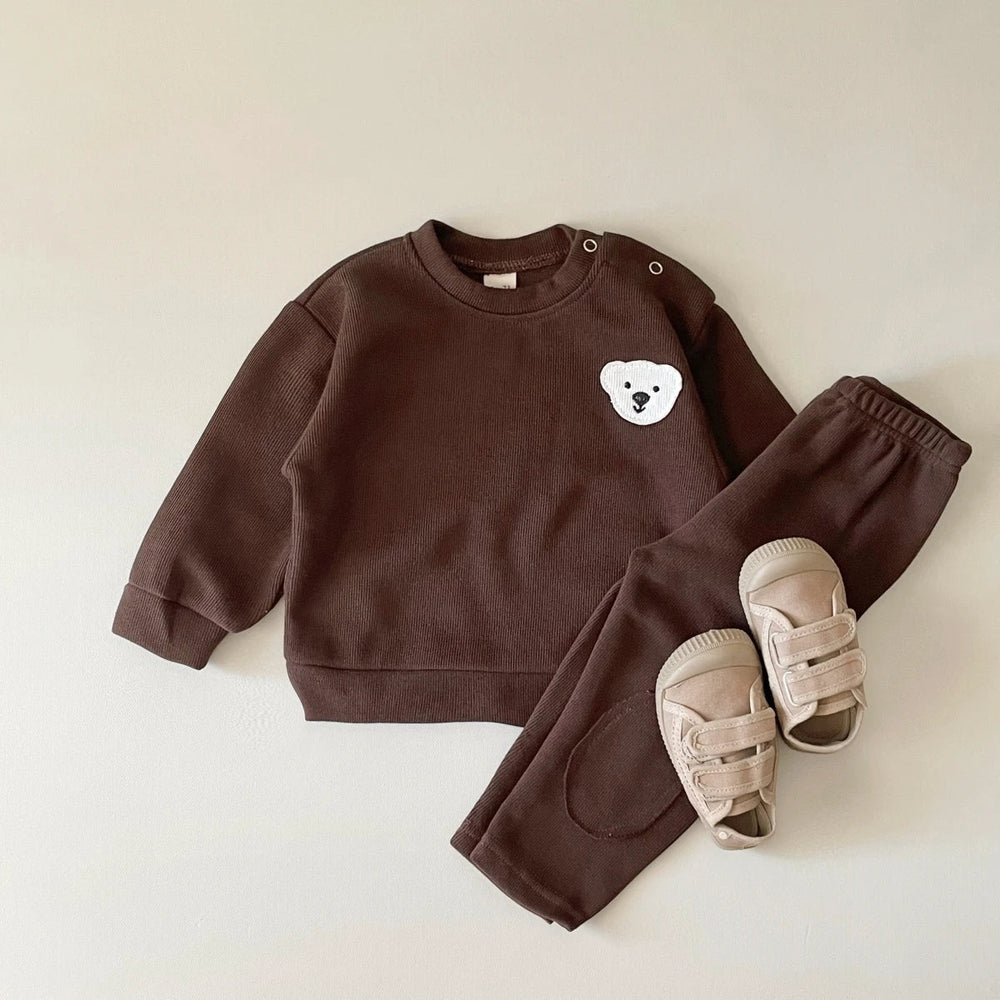 Brown bear tracksuit laid flat with a long-sleeve sweater, matching pants and beige sandals