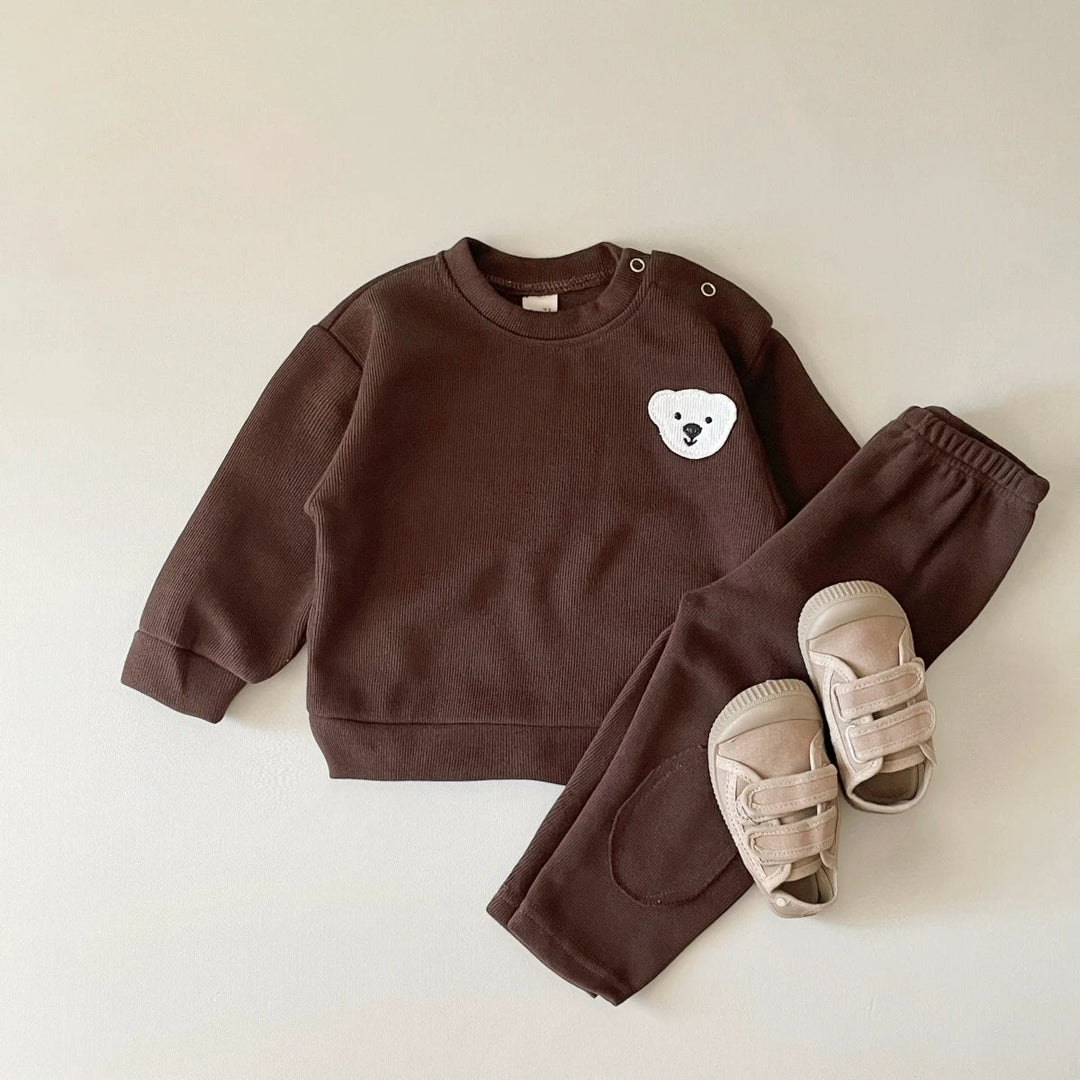 Brown bear tracksuit laid flat with a long-sleeve sweater, matching pants and beige sandals