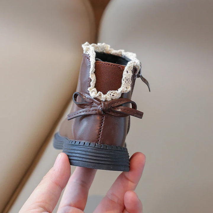 Back of a brown ankle boot with a decorative bow and cream ankle trim