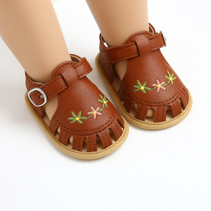 Brown baby sandals with floral embroidery and adjustable straps on mannequin feet