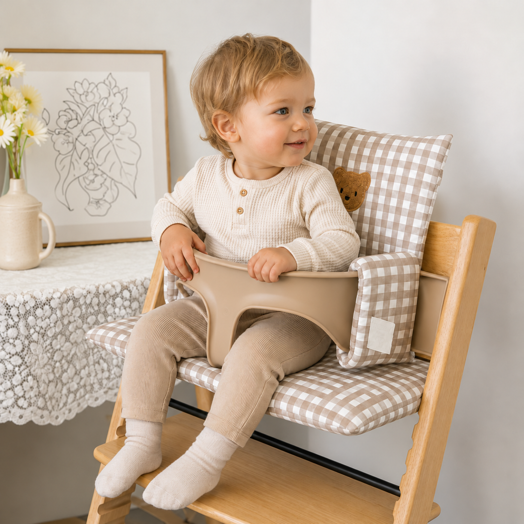 Child sitting on a brown gingham bear cushion in a wooden high chair beside the dining table