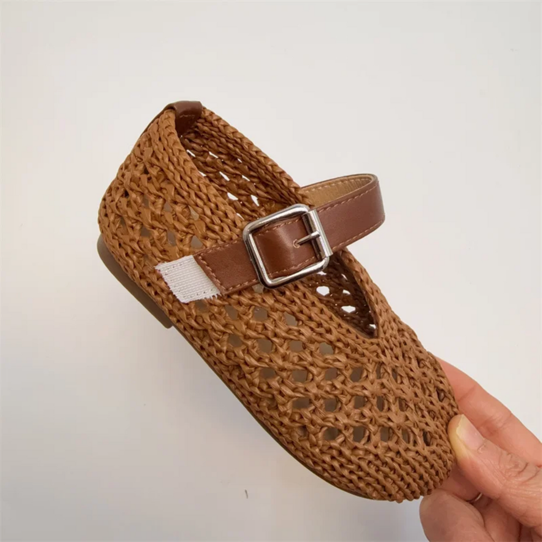 Brown Mary Jane flat held at an angle to show the woven upper and buckle strap