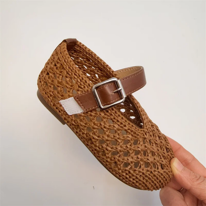 Brown Mary Jane flat held at an angle to show the woven upper and buckle strap