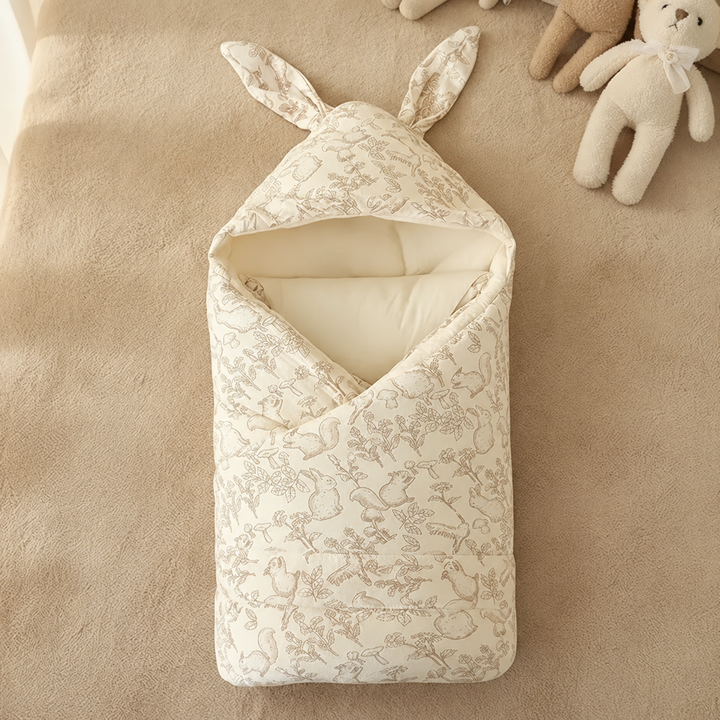 Bunny-print swaddle blanket arranged beside soft toys on a beige surface