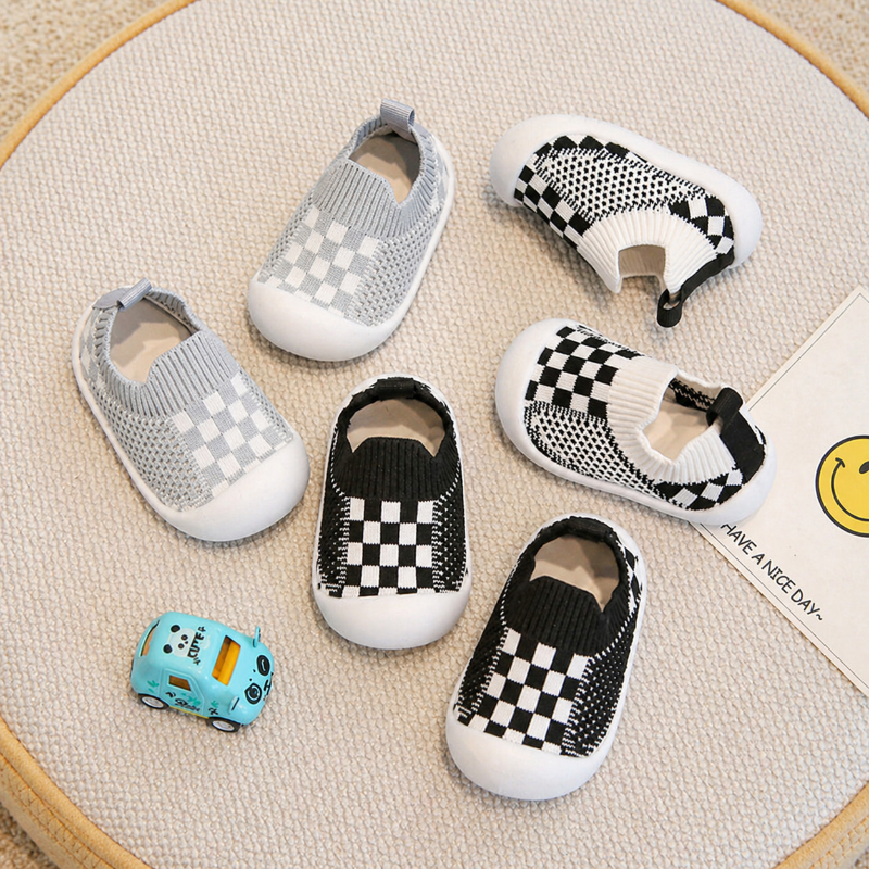 Gray, black, and white checkerboard baby sock shoes with ribbed cuffs and white soles.