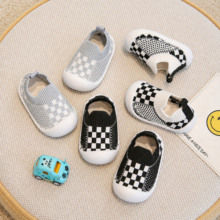 Gray, black, and white checkerboard baby sock shoes with ribbed cuffs and white soles.