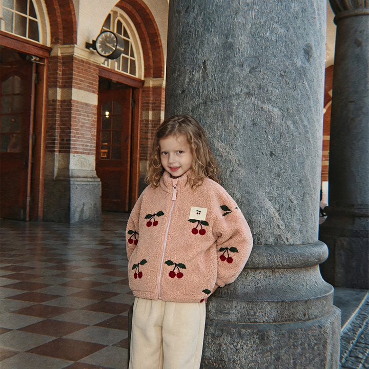 Child wearing a zipped pink cherry-print fleece jacket with light pants