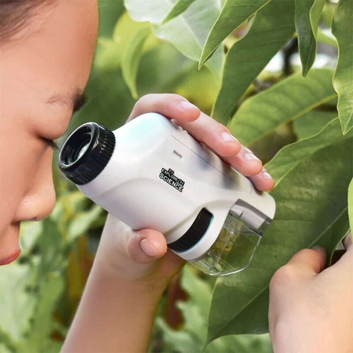 Child using a white pocket microscope to examine a leaf outdoors.