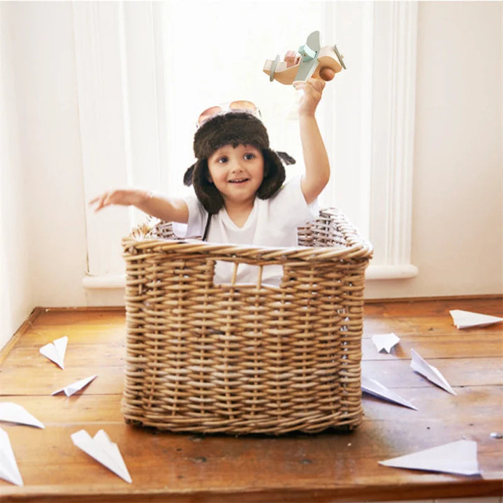 Child in a wicker basket holding a wooden toy airplane overhead